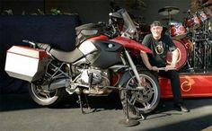 a man standing next to a red motorcycle in front of a drum set and drums