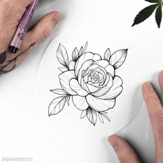 a person drawing a flower on top of a piece of paper next to a marker pen