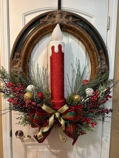 a christmas wreath with a red candle and evergreens is hanging on the front door