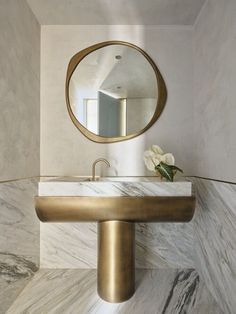 a bathroom with marble counter top and gold faucet in front of a round mirror