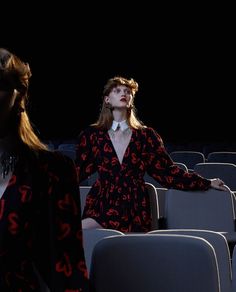 two women in black and red dresses standing next to each other at an empty theater