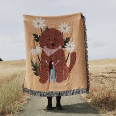 a person standing in front of a brown teddy bear with daisies on it's back