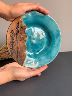 two hands are holding a blue plate with an image of trees and leaves on it