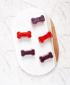 four dog bone shaped gummy treats on a white plate next to a wooden spoon