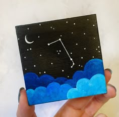 a person holding up a small painting with a sky background and stars in the sky