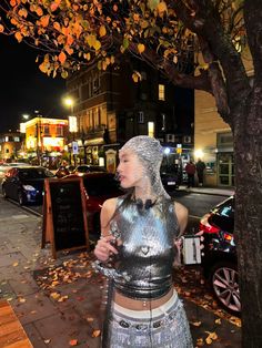 a woman dressed in silver standing next to a tree