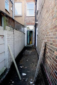 an alley way with brick walls and broken doors on both sides, leading to another building