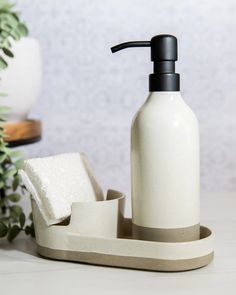 a white soap dispenser sitting on top of a counter next to a plant