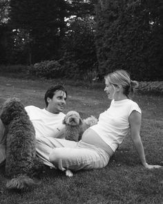 a man and woman sitting on the grass with a dog in front of their back