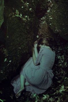 a woman sitting on the ground with her head in her hands, surrounded by leaves