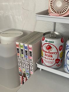 three cans of strawberry milk on a shelf next to two books and an air conditioner