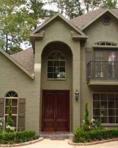 a large house with two red doors and brown shutters on the front door is surrounded by greenery