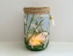 a glass jar with flowers painted on the side and rope around it, sitting on a table