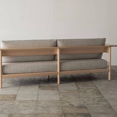 a wooden couch sitting on top of a tile floor next to a wall with two pillows