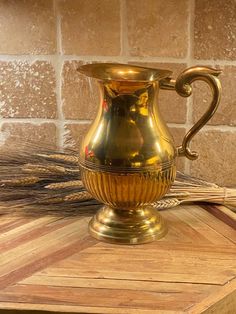 a golden vase sitting on top of a wooden table next to a brick wall and floor