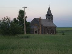 an old wooden church in the middle of a field with power lines and telephone poles