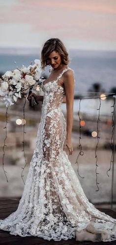 a woman in a wedding dress with flowers on her shoulder and an open back, standing near