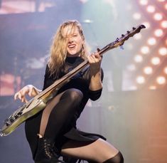 a woman in tights holding a guitar and singing into the microphone at a concert