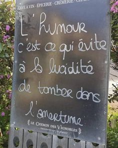 a sign that is written in french on the side of a wooden fence with purple flowers behind it