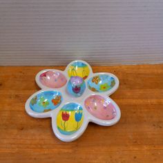 four flower shaped dishes sitting on top of a wooden table next to a white wall