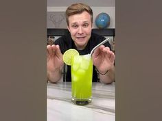 a man holding up a green drink with a lime slice on the rim in front of him