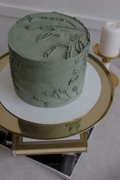 a green cake sitting on top of a gold platter next to a white candle