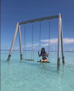 a woman is sitting on a swing in the middle of the ocean with clear blue water