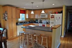 a kitchen with wooden flooring and white appliances on the counter top, along with bar stools