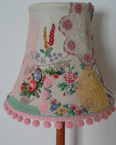 a pink lamp shade with flowers and lace on the bottom is hanging from a wooden pole