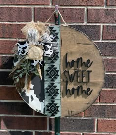 a sign that says home sweet home hanging on the side of a brick wall next to a plant