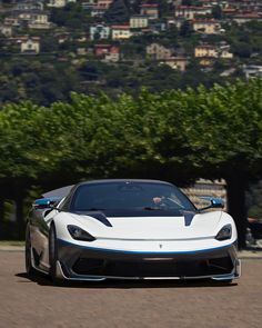 a white and blue sports car driving down a road next to a lush green hillside