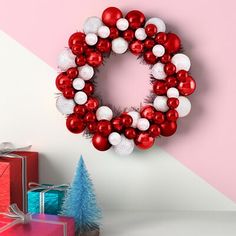 a christmas wreath with red and white balls hanging on the wall next to gift boxes