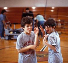 two young boys standing next to each other on a basketball court with their hands in the air