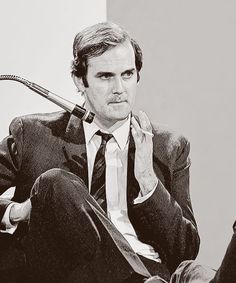 a black and white photo of a man sitting in a chair with a pipe sticking out of his mouth