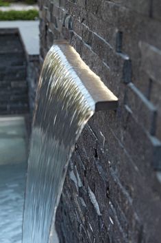 a water fountain spouting from the side of a brick wall next to a pool