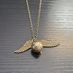 a gold necklace with an angel wing and a glass ball in the middle on a wooden surface