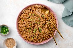 a pink bowl filled with noodles and chopsticks on top of a white table