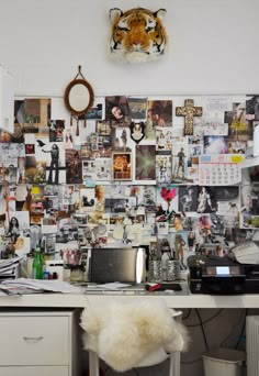 a white desk topped with a laptop computer next to a wall covered in pictures