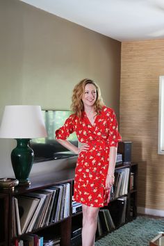 a woman in a red dress standing next to a bookshelf full of records