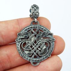 a hand holding a silver pendant with an intricate design