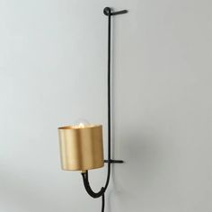 a wall light with a gold shade hanging from it's side on a white wall