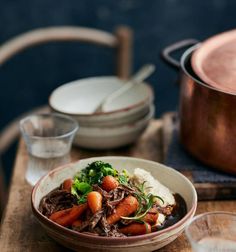 a bowl filled with meat and vegetables on top of a wooden table