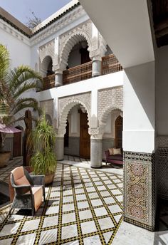 an outdoor courtyard with chairs and potted plants in the center, surrounded by white walls