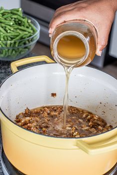 someone pouring sauce into a pot filled with green beans