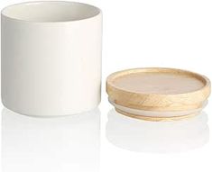 a white cup with a wooden lid next to a round container on a white surface