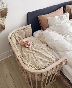 a baby in a crib next to a bed with pillows and blankets on it