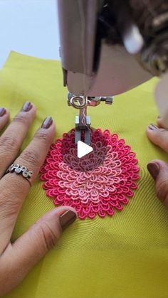 two hands are using a sewing machine to sew on a yellow table cloth with red and pink crocheted doily