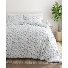 a white bed with blue flowers on it in a room next to a potted plant