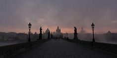 people walking across a bridge at dusk with the sun going down in the distance,