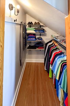 an open closet with clothes and shoes hanging on the wall, next to a wooden floor